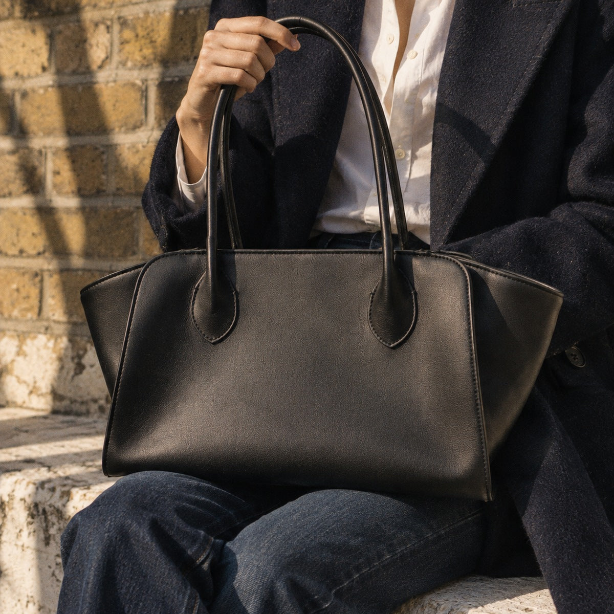 Black winged leather tote bag held on the lap, London townhouse brick in low autumn sun